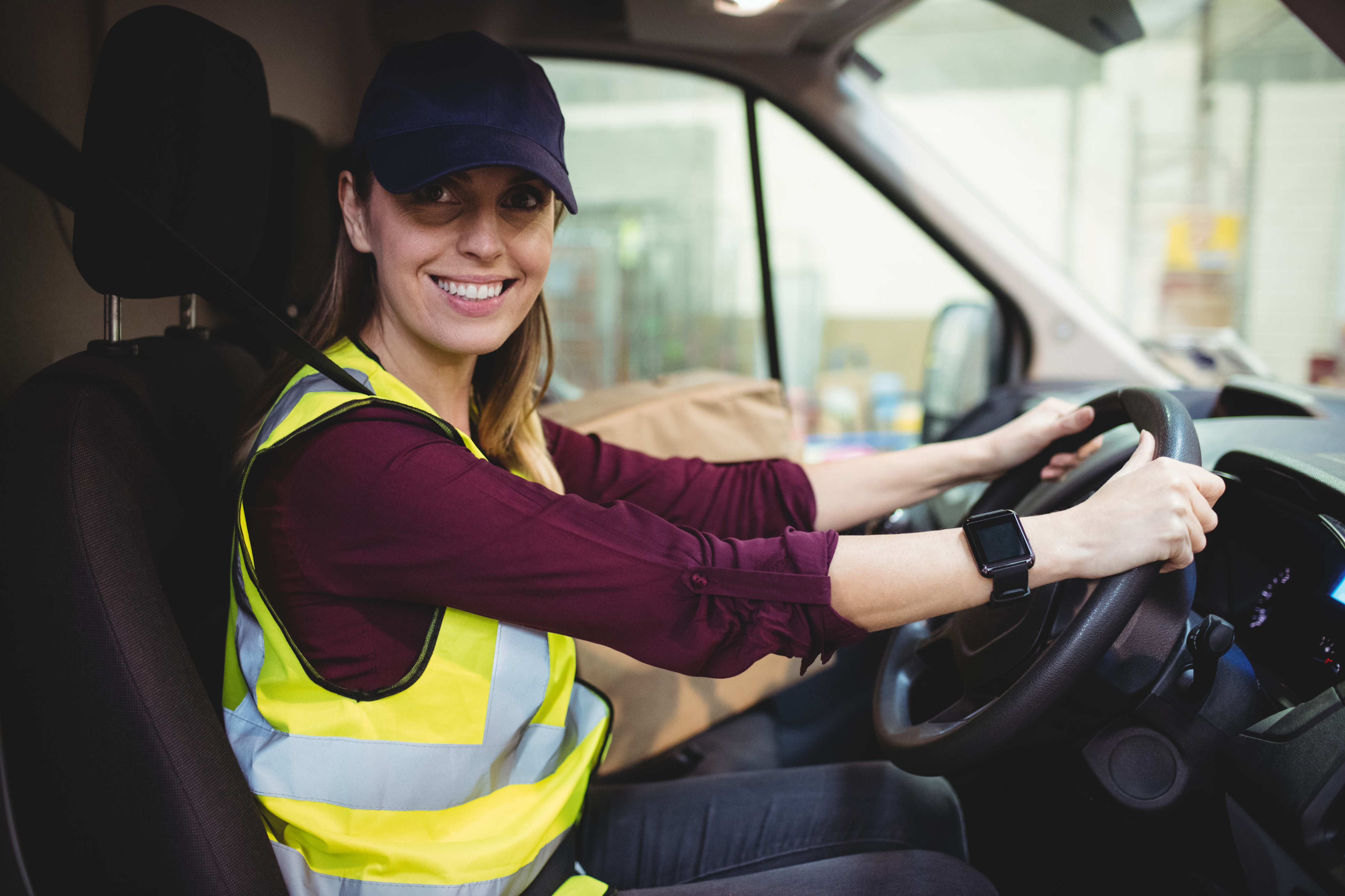 Delivery driver driving van with parcels on seat outside warehouse